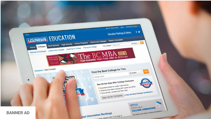 Person holds a tablet displaying a college ranking website. The screen shows various ranking categories for educational institutions, with a banner ad for an MBA program visible at the top. The user's hand points to one of the ranking categories on the screen.